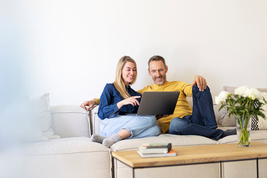 Smiling couple uses a laptop on the sofa in the living room