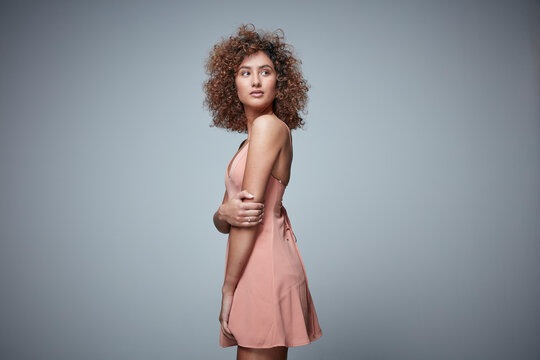 Portrait of redheaded woman with curly hair wearing salmon coloured dress