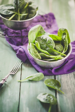 Bowl of fresh spinach leaves on cloth and wood