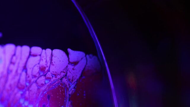 Glowing violet fluid film with intricate cellular marbling. Vibrant violet and magenta backlighting illuminates a horizontal liquid plane boundary.