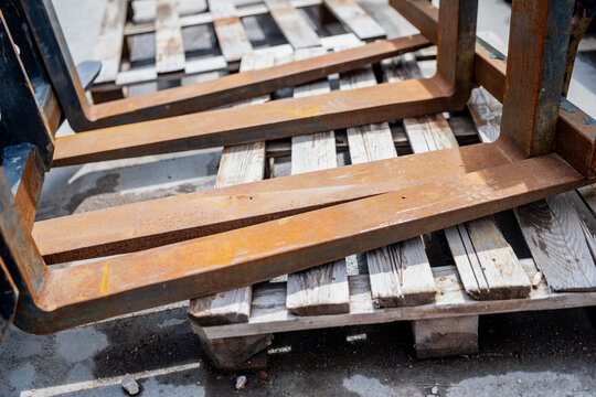 Rusty steel forklift attachment tines stored on a timber pallet for material handling and warehouse supply logistics
