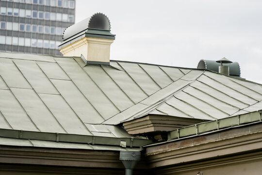 Green painted standing seam metal roofing system featuring rendered stucco chimney stacks with decorative arched metal cowls