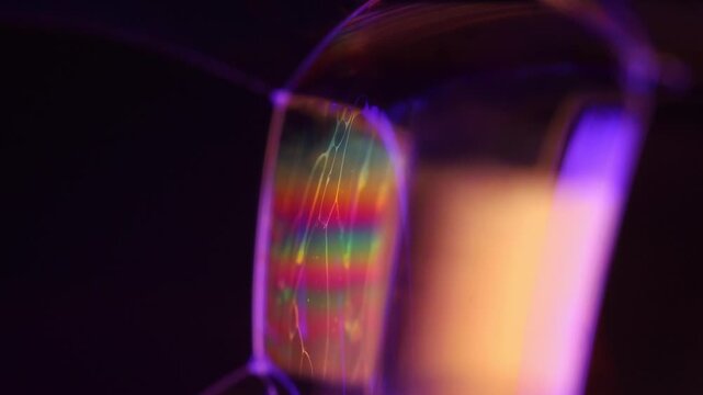 Geometric liquid film cell with rainbow interference bands and violet frame. Crisp violet specular rim lines define a multi-faceted liquid film structure in low-key macro perspective