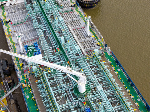 Aerial view of an industrial oil tanker deck featuring complex piping systems, industrial equipment, and workers in high-visibility gear in the United Kingdom.
