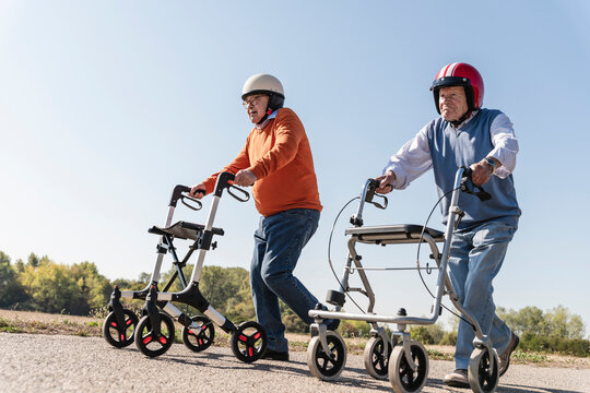Two old friends wearing safety helmets, competing in a wheeled walker race