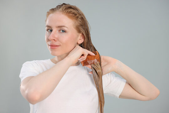 Woman brushing hair after applying mask on light grey background