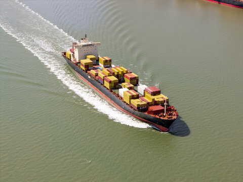 Aerial view of a large container ship loaded with colorful shipping containers moving through calm water leaving a white wake in the United Kingdom.