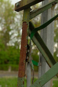 Worksite detail patched rusted pole with wiring and clamp near roadside, weathered metal bearing repair marks and grit portrays temporary field fix