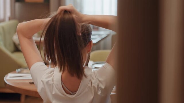 Woman styling hair into bun during evening prep, intimate dining room backdrop with soft ambient light, practicing updo technique with pins and clips, focused hands and confident ritual