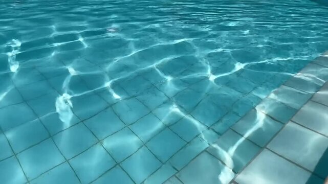 Sunlight reflecting on the turquoise tiled bottom of a clear swimming pool with ripples