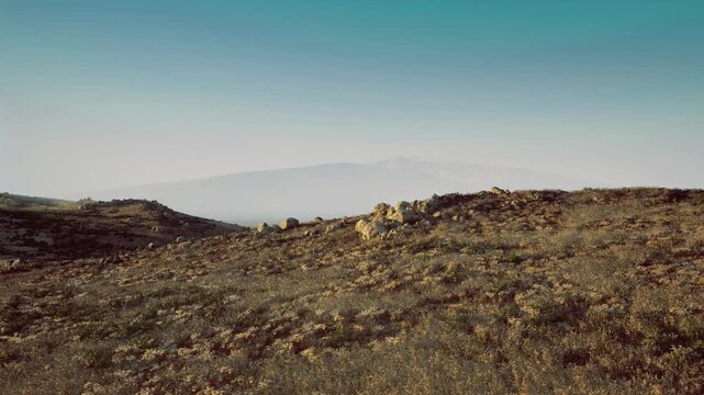 Expansive rocky terrain with distant mountain silhouette, clear teal sky and scattered boulders, visual narrative suitable for route planning, outdoor logistics