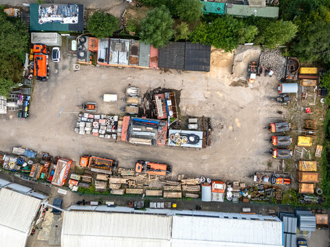 Aerial view of construction material storage yard with stacks of timber, pipes, and various building supplies arranged on a gravel lot in Germany.