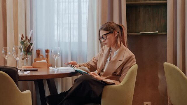 Female author engrossed in thoughtful solitude. Caucasian female writer lost in introspective binge by window. Solitary woman novelist contemplates with focus in peaceful bistro ambiance