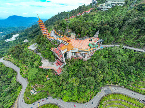 Aerial view of the Chin Swee Caves Temple with its iconic pagoda and large Buddha statue amidst lush mountain forests and winding roads in Genting Highlands, Pahang, Malaysia.