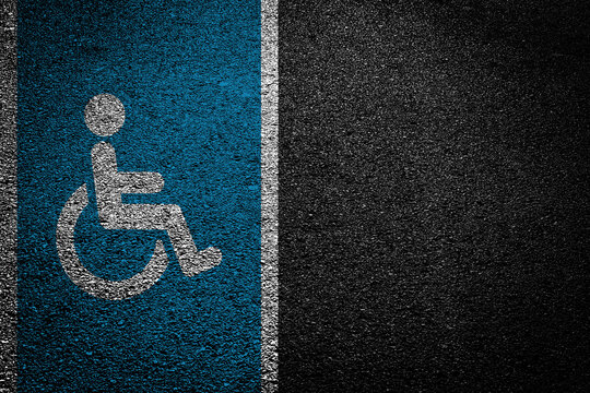 Disabled parking symbol on asphalt. Blue wheelchair sign painted on road. Accessible parking space marking outdoors. Urban street surface detail. Public accessibility infrastructure. Safety rules zone