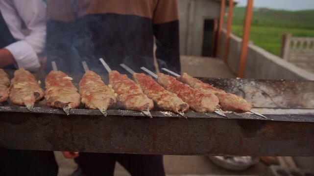 Slow motion camera panning of traditional lula kebab shashlik grilling on skewers over a mangal with smoke at an outdoor restaurant, horizontal video.