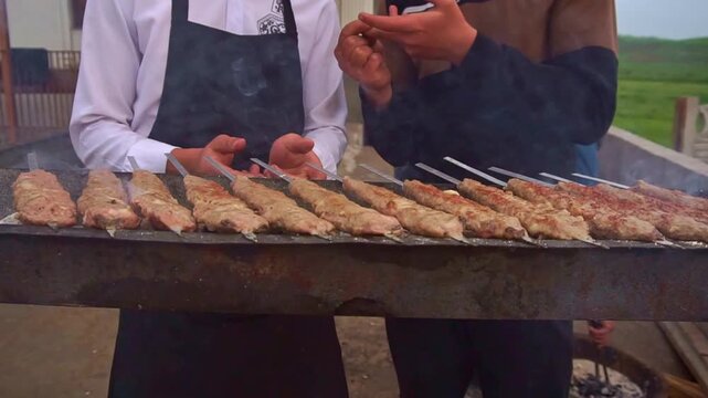 Slow motion camera panning of traditional lula kebab shashlik grilling on skewers over a mangal with smoke at an outdoor restaurant, horizontal video.