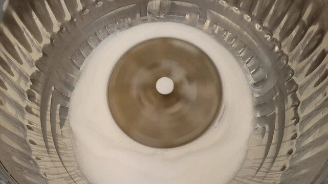 Top down view of washing machine agitator spinning . Rapidly rotating pulsator in laundry washer with soapy water
