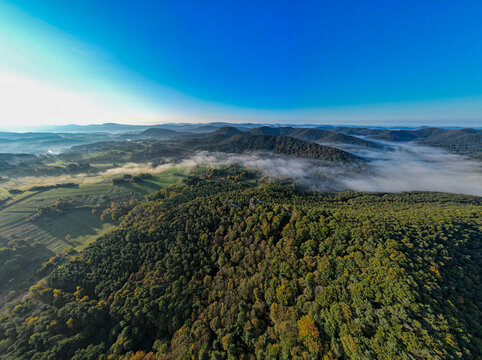 Aerial view of the forested hills and valleys near Wernersberg, with morning mist settling in the lowlands in Wernersberg, Rhineland-Palatinate, Germany.
