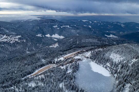 Aerial view of Mummelsee lake surrounded by snow-covered Black Forest trees and mountains under a cloudy sky in Seebach, Baden-Wurttemberg, Germany.