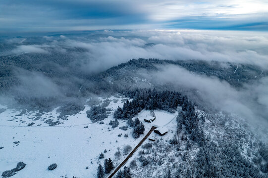Aerial view of Mummelsee area in winter with snow-covered pine trees and a small cabin nestled in the landscape, Seebach, Baden-Wurttemberg, Germany.