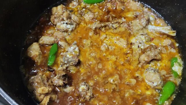 Delicious chicken curry simmering in a black pot . Traditional spicy chicken karahi with green chilies
