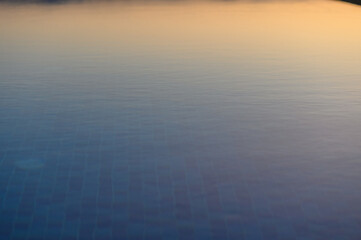 Tranquil water surface reflects the colors of the sunset over a serene landscape