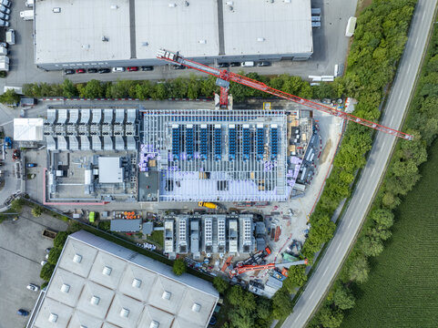 Aerial view of the Portus Data Centers construction site featuring a large crane, industrial framework, and cooling units in Kirchheim bei Muenchen, Bavaria, Germany.
