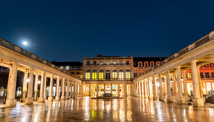 Fototapeta premium Illuminated colonnades and courtyard of the historic Palais Royal at night with reflections on wet ground in Paris, France.