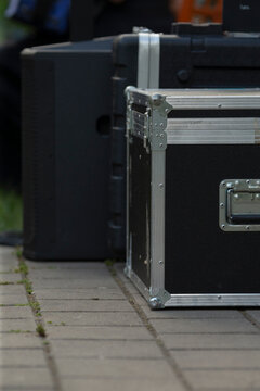 Closeup equipment case on pavement showing rugged handle and latch, metallic corner protectors, stacked flightcase beside speaker roadcase, urban