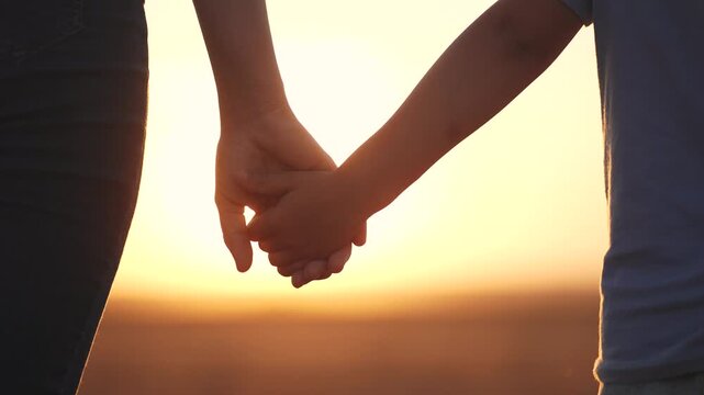 A person holding hands in the sunset. Mom, holds, daughter, hands walk, park. Mom and daughter walking in the park. The photo is of a mother and child holding hands at sunset lifestyle.