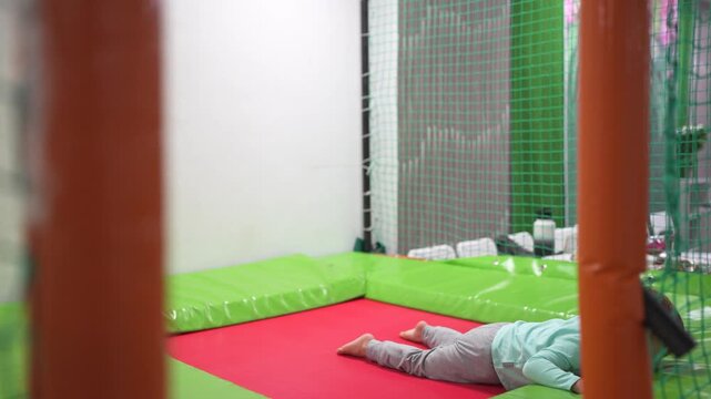 A young child playing on an indoor trampoline. Child, boy, jumping, trampoline, playroom, kid, play, happy. Happy kids playing in a playroom. Describe lifestyle.
