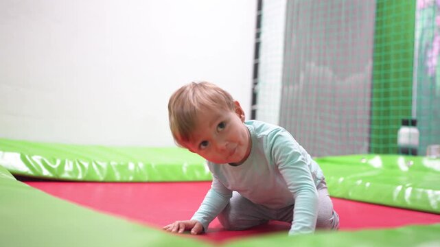 A young child playing on an indoor trampoline. Child, boy, jumping, trampoline, playroom, kid, play, happy. Happy kids playing in lifestyle a playroom. Describe.