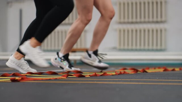 Rhythmic ladder warmup for badminton players, duo performing synchronized hops and quickstep drills across agility ladder, shoes scuffing court surface, upbeat tempo and endurance focus