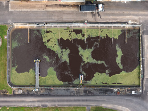 Aerial view of the solar powered waste water treatment plant with dark water, green algae, metal walkways, and surrounding paved infrastructure in Byron Bay, New South Wales, Australia.