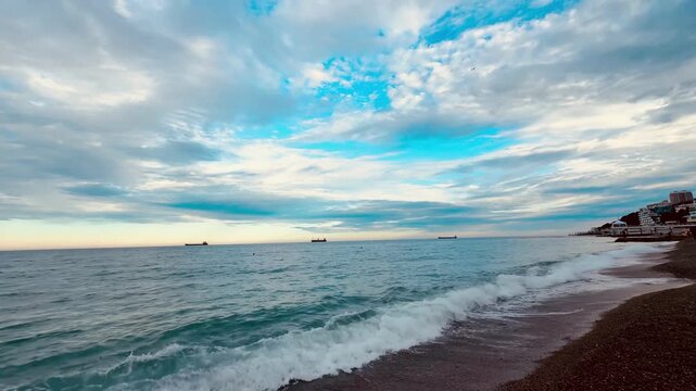 Gentle waves on a pebble beach, cargo ships on the horizon and dramatic sunset clouds