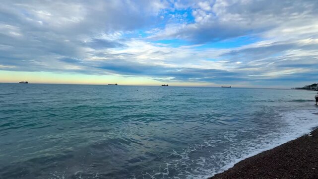 Gentle waves on a pebble beach, cargo ships on the horizon and dramatic sunset clouds