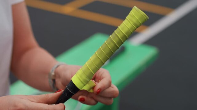 Closeup hands wrapping badminton racket grip bench scene neon yellow overgrip applied with precise fingers blurred court lines equipment maintenance focus stepbystep method for durable comfortable