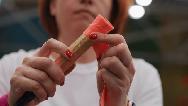 Detailed sports scene. Player wrapping sport tape around racket handle meticulously in gym. Female athlete preparing her badminton racket with fresh grip tape before training session