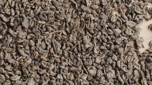 Green dried gunpowder chinese tea leaves with scoop on white wooden background, closeup.