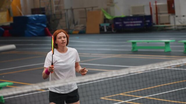 Focused white player playing badminton with determined expression on indoor court, club competitor hitting precise shots and returns, tactical movement, redhead competitor energy, matchlike intensity
