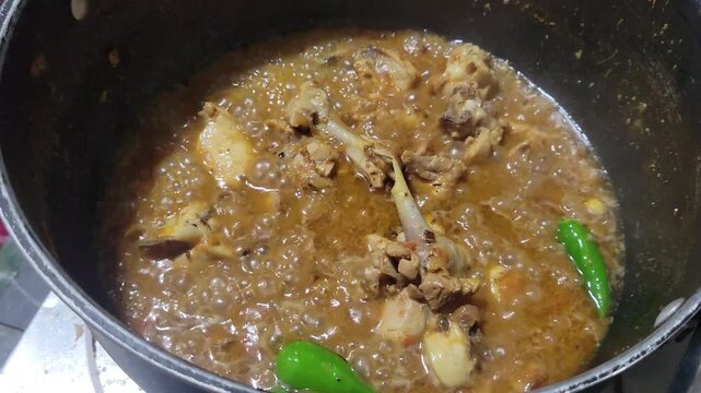 Delicious chicken curry with green chilies simmering in a pot . Spicy chicken gravy bubbling in a black cooking pot
