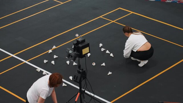 Partners sort shuttlecocks after training session on court, collaborative cleanup and coaching feedback with camera setup, attentive instruction and review create calm postpractice atmosphere