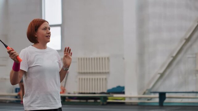 Refining indoor badminton skills. Casual solo session improves shuttlecock control and stance. Player in casual attire hones badminton serve technique with gentle wrist movements and balance