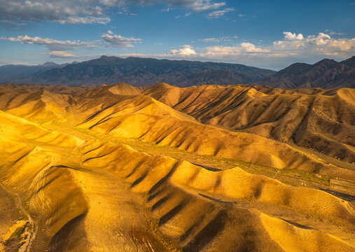 Aerial view of golden rolling hills and rugged mountain terrain under a clear blue sky in Naryn, Naryn Region, Kyrgyzstan.