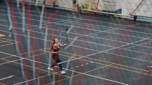 Solo badminton footwork drill on court with single player practicing precise swings, shuttlecock handling and timing, concentrated stance and repetition, gym floor markings and camera angle emphasize