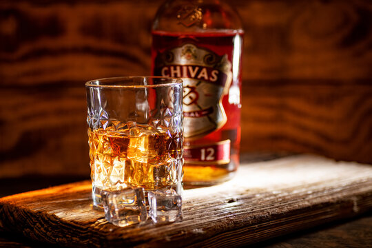 Chivas Regal 12 whisky glass glows against a softly blurred bottle background.