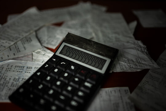 Horizontal close-up of a calculator displaying numbers over scattered bills in dark lighting