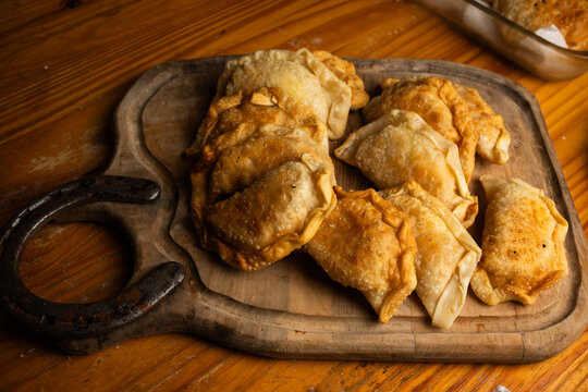 Freshly cooked homemade empanadas piled on a wood platter over a table