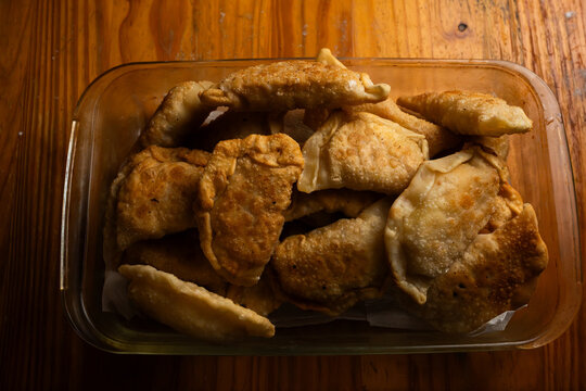 Top view of freshly fried golden brown empanadas piled in a glass baking dish